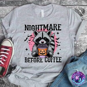 May include: Gray t-shirt with a raccoon holding a pumpkin spice latte. The text "Nightmare Before Coffee" is printed on the shirt.