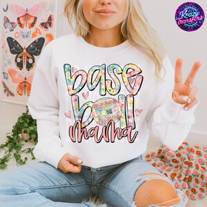 Könnte beinhalten: Weißer Pullover mit einem floralen Design, auf dem "Baseball Mama" mit einem Baseball in der Mitte steht.