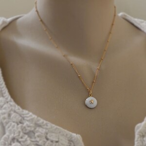 May include: A gold chain necklace with a small white pendant featuring a gold star. The necklace is on a white mannequin.