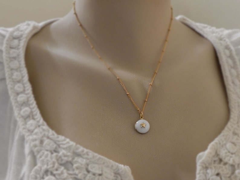 May include: A gold chain necklace with a small white pendant featuring a gold star. The necklace is on a white mannequin.