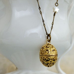 May include: A gold filigree pendant necklace with a white star charm. The pendant is shaped like an egg and has a delicate, intricate design.