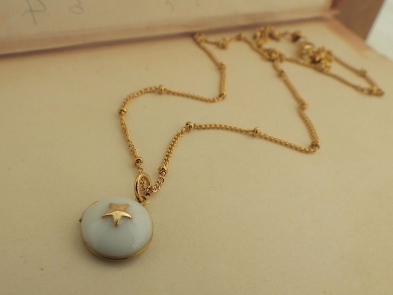 May include: A gold chain necklace with a white enamel pendant featuring a gold star.
