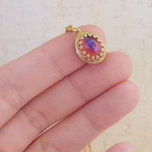 May include: A gold pendant necklace featuring a red and purple oval-shaped stone set in a gold filigree frame.