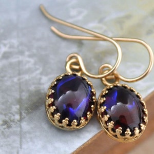 May include: A pair of gold earrings with a dark blue oval gemstone set in a gold filigree frame.