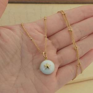 May include: A gold chain necklace with a small white pendant featuring a gold star. The chain is made of small gold beads.