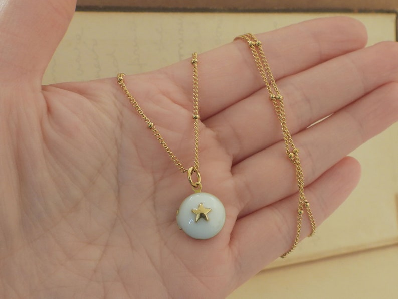 May include: A gold chain necklace with a small white pendant featuring a gold star. The chain is made of small gold beads.