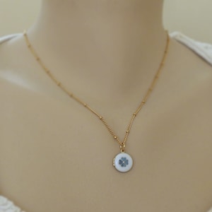May include: A gold chain necklace with a small round locket pendant featuring a white enamel four-leaf clover design.