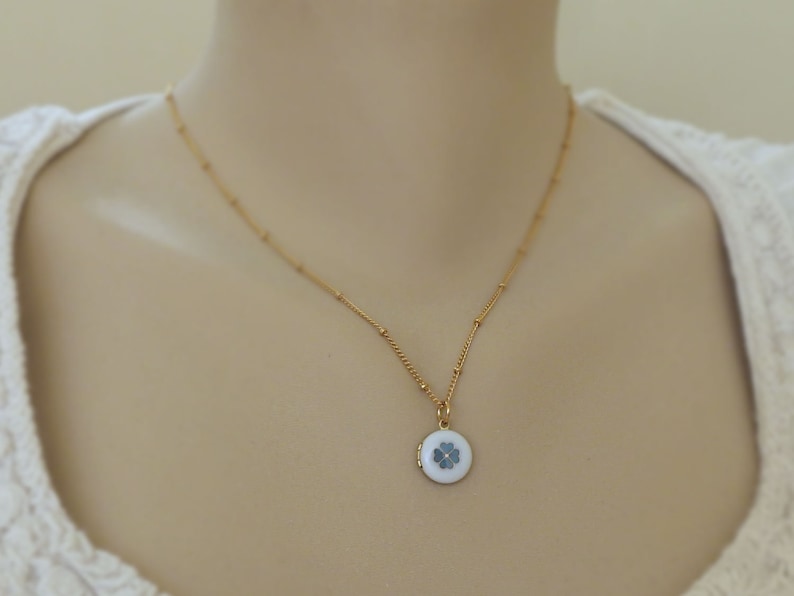 May include: A gold chain necklace with a small round locket pendant featuring a white enamel four-leaf clover design.