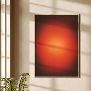 May include: A rectangular wall art piece featuring a gradient design that transitions from a deep, dark red at the edges to a bright, glowing orange center, enclosed within a thin, light-colored wooden frame hanging on a neutral wall.