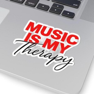 May include: A white sticker with the text "MUSIC IS MY Therapy" in red and black. The words "MUSIC IS MY" are in a bold, blocky red font, while "Therapy" is in a cursive black font.