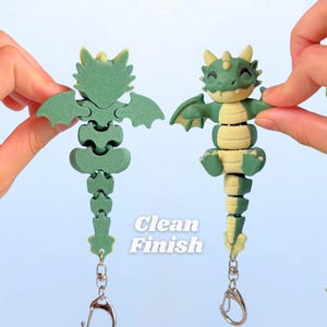 May include: Two articulated dragon keychains. One is fully assembled, the other is a skeleton. The dragons are green and yellow with silver key rings. The text "Clean Finish" is printed on the image.
