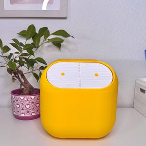 Könnte beinhalten: Ein leuchtend gelber, rechteckiger Schreibtisch-Organizer mit einer weißen, geschlitzten Oberseite. Der Organizer steht auf einem weißen Schreibtisch, neben einer kleinen Topfpflanze und einem Stifthalter mit bunten Stiften.