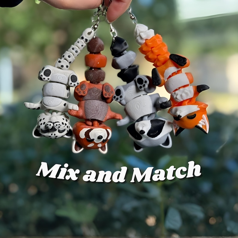 Four 3D printed articulated flexi keychains hanging together — Leopard, Red Panda, Raccoon, and Classic Orange Fox — showing how different animals pair and collect beautifully. Each has unique colors and detailed segmented bodies. Text overlay reads Mix and Match. Animal keychain collection 3D printed flexi fox raccoon leopard red panda bag charm mix match gift set