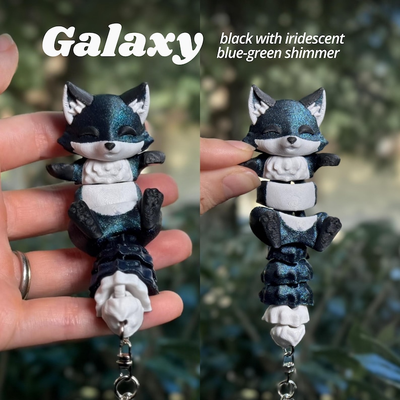 Galaxy colorway 3D printed flexi fox keychain from two angles. Deep black base with a mesmerizing iridescent blue-green shimmer that shifts and glows at every angle. Fully segmented articulated body with white facial markings and white belly. Galaxy fox keychain dark 3D printed fidget bag charm blue shimmer black fox articulated backpack charm fidget toy fox lover gift cute animal keychain