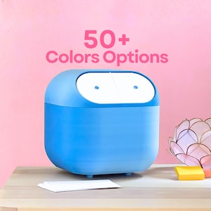 Puede incluir: Un contenedor azul claro y redondeado con una parte superior blanca y el texto "50+ Colors Options" en rosa. El contenedor está sobre una superficie de madera contra un fondo rosa. Varias tarjetas blancas pequeñas están frente al contenedor.