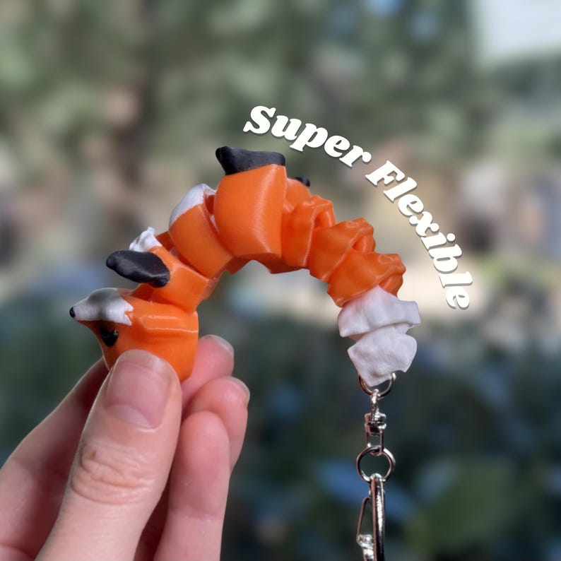 Classic Orange 3D printed articulated fox keychain bent into a wide arch to show maximum flexibility. Each segment of the body bends independently — torso, legs, and tail all move freely at every joint. A satisfying sensory fidget toy at 10cm. Text overlay reads Super Flexible. Flexi fox keychain fidget toy articulated fox bag charm backpack charm 3D printed sensory fidget