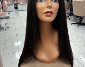 May include: A mannequin head with long, straight, dark brown hair. The mannequin has a neutral skin tone, with makeup including pink eyeshadow and red lipstick. The mannequin is placed on a tan stool in a salon setting.