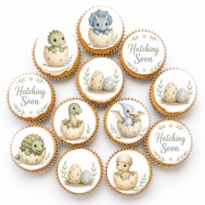 May include: A collection of eleven round cupcake toppers featuring watercolor illustrations of baby dinosaurs hatching from speckled eggs and the text Hatching Soon surrounded by green leafy branches and small orange hearts on a white background.