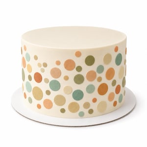 May include: A cylindrical cake with smooth off-white frosting decorated with a scattered pattern of flat, circular confetti pieces in muted shades of sage green, terracotta orange, mustard yellow, and beige, resting on a round white cake board.