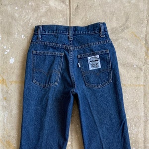 Puede incluir: Un par de pantalones vaqueros de mezclilla azul oscuro con un pequeño parche blanco en el bolsillo trasero que dice "Levi's" en blanco.