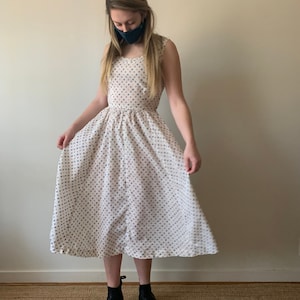 May include: A white dress with a blue and white polka dot pattern. The dress has a fitted bodice and a full skirt. The model is wearing black ankle boots.