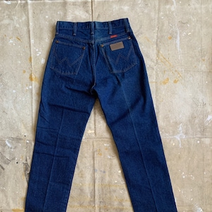 Puede incluir: Un par de pantalones vaqueros de mezclilla azul oscuro con un parche de cuero en el bolsillo trasero que dice "Wrangler".
