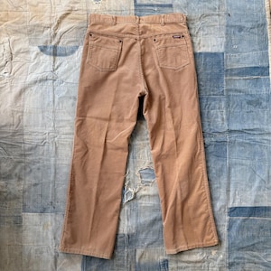 May include: A pair of brown corduroy pants with a straight leg fit. The pants have a zipper fly and button closure. The back pockets have a small leather patch with the brand name.