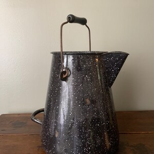 May include: Black and white speckled enamelware pitcher with a black wooden handle and a wire carrying handle.
