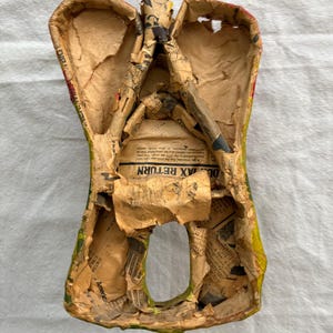 May include: A paper mache angel figure, crafted with a hollow body and wings. Constructed from newspaper, it features yellow, green, and red paint. The interior shows the layered newspaper construction, a unique craft item.