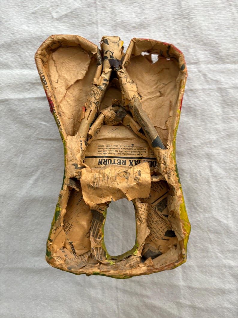 May include: A paper mache angel figure, crafted with a hollow body and wings. Constructed from newspaper, it features yellow, green, and red paint. The interior shows the layered newspaper construction, a unique craft item.