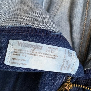 Puede incluir: Una etiqueta blanca con texto negro unida a un par de pantalones vaqueros de color azul oscuro. La etiqueta dice "Wrangler 1 MW200 9 X 32 Lavar a m&aacute;quina con colores similares, solo lej&iacute;a sin cloro cuando sea necesario, secar en secadora MADE IN USA 100% ALGOD&Oacute;N"