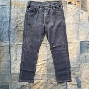May include: A pair of dark gray corduroy pants with a straight leg fit. The pants have a button fly and five pockets.