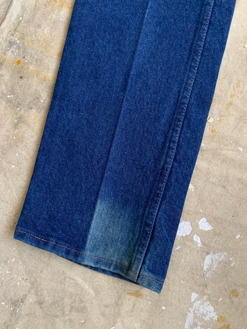 Puede incluir: Primer plano del dobladillo inferior de un par de pantalones vaqueros de mezclilla azul. Los vaqueros tienen una pierna recta y un ajuste cl&aacute;sico.