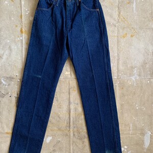 Puede incluir: Un par de pantalones vaqueros de mezclilla azul oscuro con corte recto. Los pantalones tienen un dise&ntilde;o cl&aacute;sico de cinco bolsillos y cierre de bot&oacute;n.