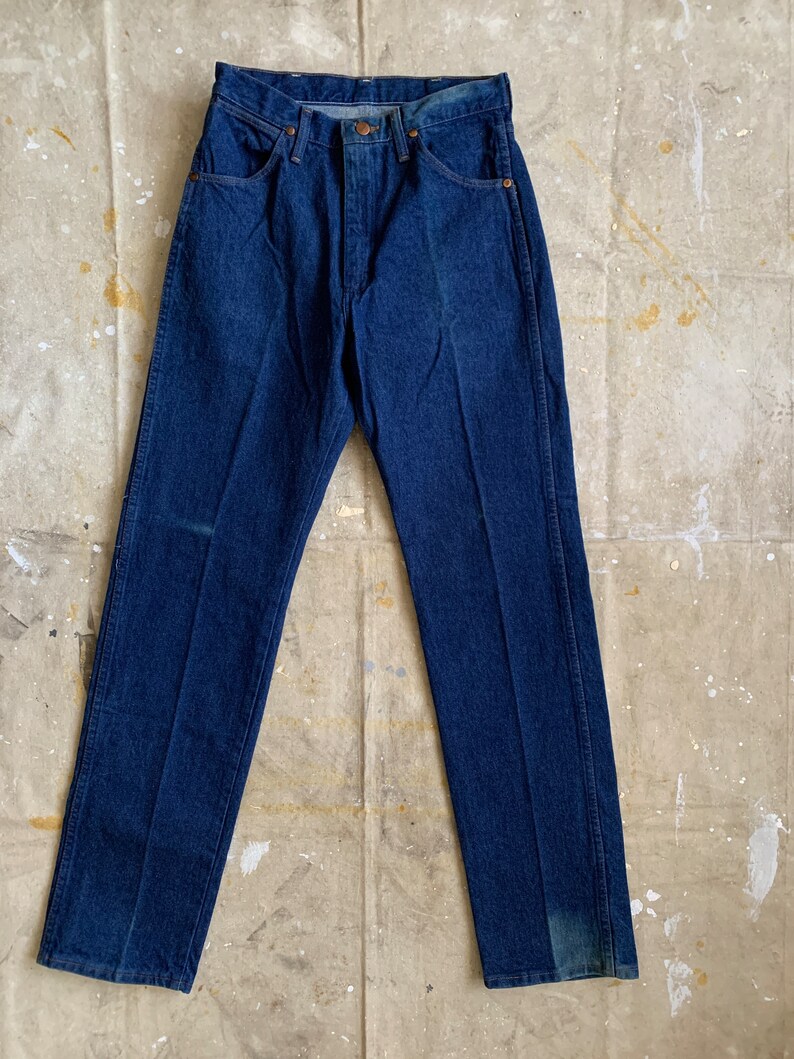 Puede incluir: Un par de pantalones vaqueros de mezclilla azul oscuro con corte recto. Los pantalones tienen un dise&ntilde;o cl&aacute;sico de cinco bolsillos y cierre de bot&oacute;n.