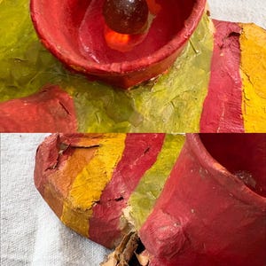 May include: A close-up of a colourful, abstract sculpture. The sculpture features a red, yellow, and green colour scheme. A small, dark, round object is visible inside a red cup-like structure. The artwork appears to be made of paper or cardboard.