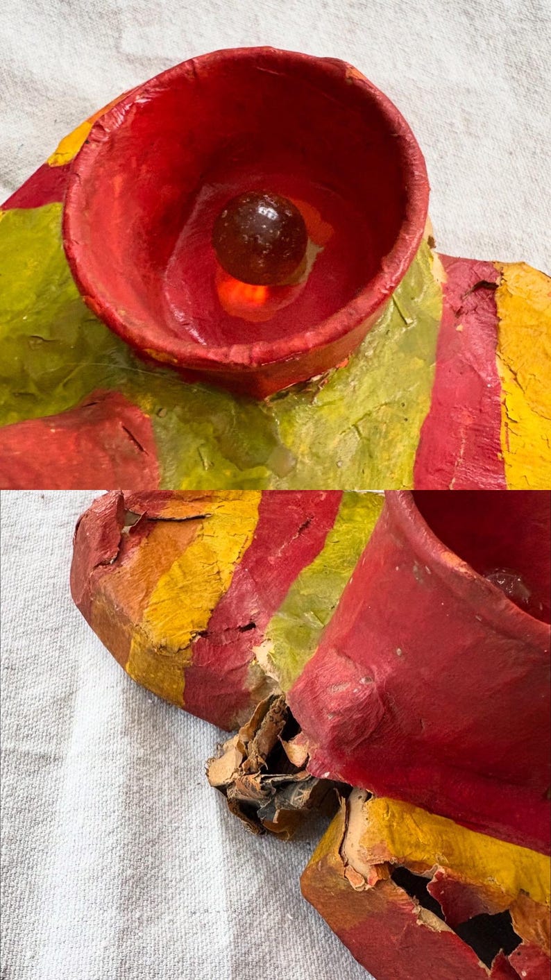 May include: A close-up of a colourful, abstract sculpture. The sculpture features a red, yellow, and green colour scheme. A small, dark, round object is visible inside a red cup-like structure. The artwork appears to be made of paper or cardboard.