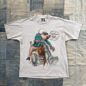 May include: A light gray t-shirt featuring a cartoon pig riding a motorcycle, wearing sunglasses and a helmet. The pig is wearing a teal jacket. Text in a speech bubble reads "Oh shit! Not another van air party!"