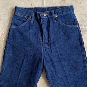 Puede incluir: Un par de pantalones vaqueros de mezclilla azul oscuro con un bot&oacute;n y remaches de cobre. Los pantalones tienen cintura alta y pierna recta.