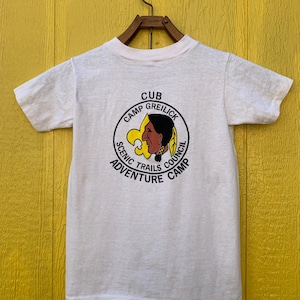 Könnte beinhalten: Weißes T-Shirt mit einem gestickten gelben und schwarzen Aufnäher mit der Aufschrift "Cub Camp Greilick Scenic Trails Council Adventure Camp".