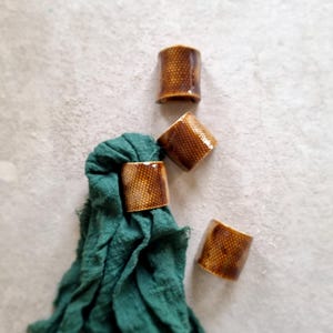 Könnte beinhalten: Set aus vier braunen Keramik-Serviettenringen mit einem Wabenmuster. Die Ringe liegen auf einer grünen Stoffserviette.
