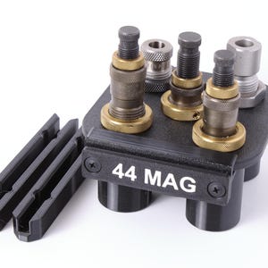 May include: A black metal reloading tool holder with "44 MAG" in white text. It holds several reloading dies with brass and silver accents. Two black plastic holders are on the left.