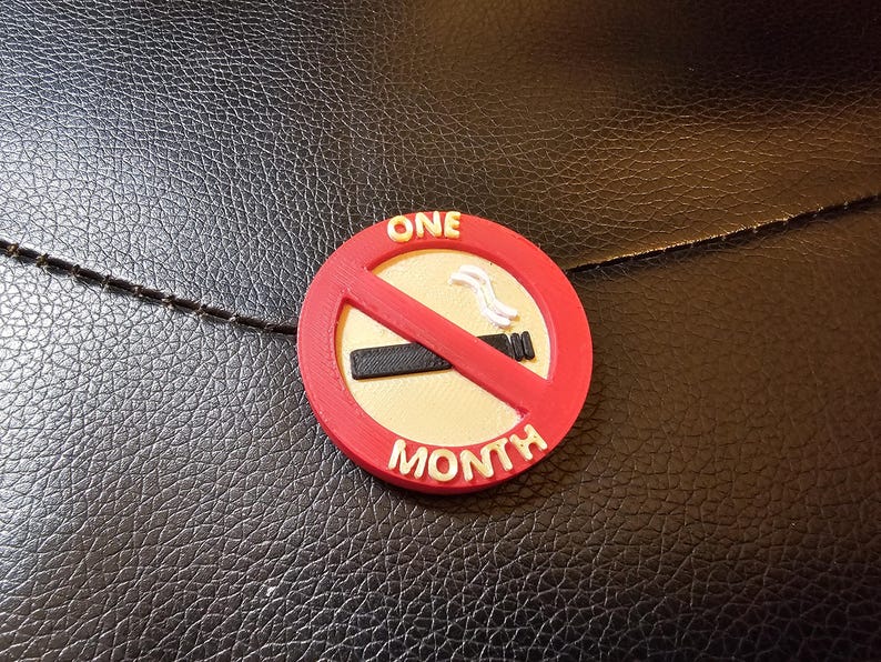 May include: A red, white, and black circular emblem with the words "ONE MONTH" and a no-smoking symbol. The emblem is on a textured black surface.
