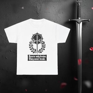 May include: White t-shirt with a black graphic of a sword through a floral wreath, with the text "Hearts only bruise. They never break." A silver sword is positioned to the right of the shirt.