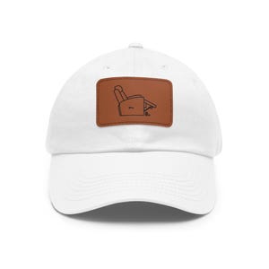 Puede incluir: Gorra de béisbol blanca con un parche de cuero marrón con un dibujo lineal negro de un sillón reclinable. La gorra tiene una visera curva y un diseño clásico de seis paneles.
