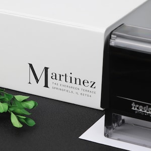 Könnte beinhalten: Ein weißer selbsttinte­nder Adressstempel mit dem Text "Martinez 742 Evergreen Terrace Springfield, IL 62704" darauf gedruckt.