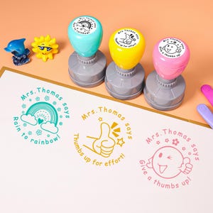 May include: Three colorful teacher stamps with the text "Mrs. Thomas says" and various phrases. The stamps are teal, yellow, and pink. The stamped images include a rainbow, a thumbs up, and a smiling face.