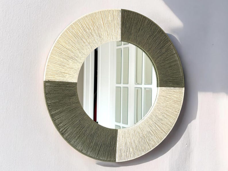 Pode incluir: Um espelho de parede circular com uma moldura envolta em segmentos alternados de fio cor de creme e verde-azeitona. O fio &eacute; enrolado firmemente &agrave; volta da borda circular, criando um padr&atilde;o radial texturado que rodeia a superf&iacute;cie refletora.