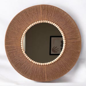 May include: A round mirror with a brown woven frame and a border of natural wood beads.