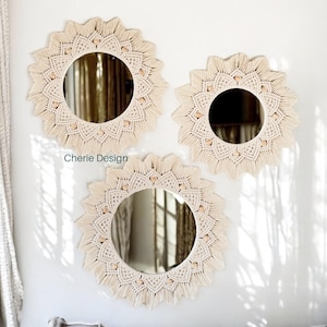 May include: Three circular wall mirrors featuring intricate cream-colored macrame borders with knotted patterns and small wooden beads. The mirrors are arranged in a cluster, and the text Cherie Design is visible near the upper left mirror.